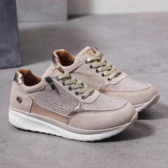 Paar beigefarbene Sneaker mit goldenen Schnürsenkeln, Strassbesatz und weißer Sohle, ohne Model auf grauem Boden aufgestellt. 2