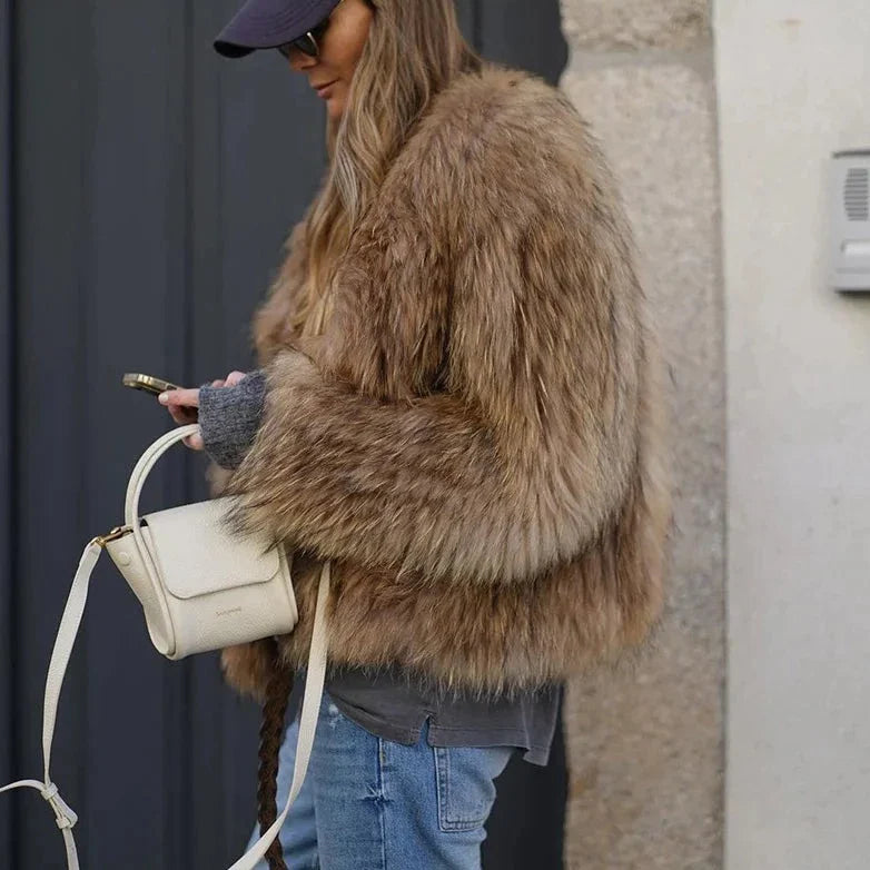 Frau mit brauner Kunstpelzjacke, blauer Jeans, weißer Tasche, Smartphone, draußen.