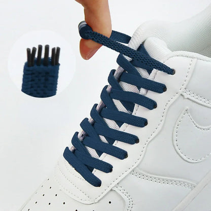 Dunkelblaue flache Schnürsenkel an einem weißen Sneaker, eine Hand zieht an der Kapsel, Detailansicht der Enden 1
