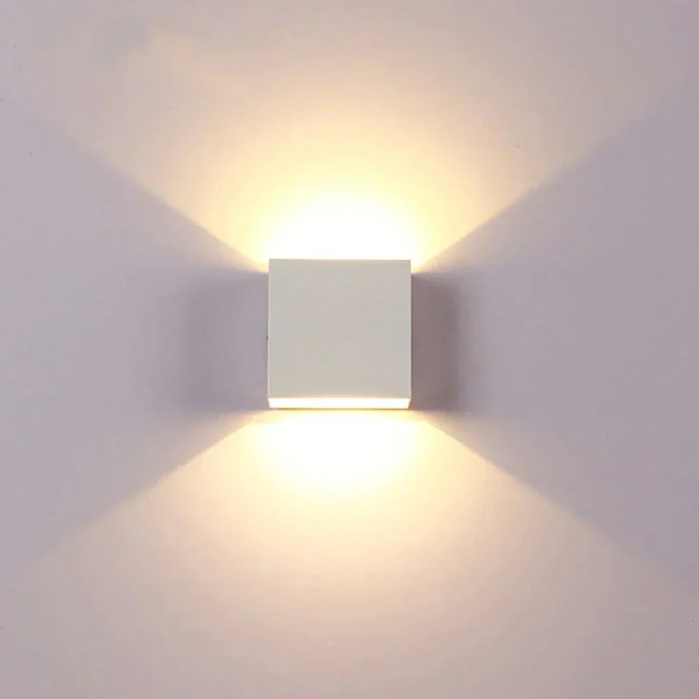 Weiße Würfel-Wandlampe frontal an heller Wand, warmes Licht strahlt gleichmäßig nach oben und unten. 17