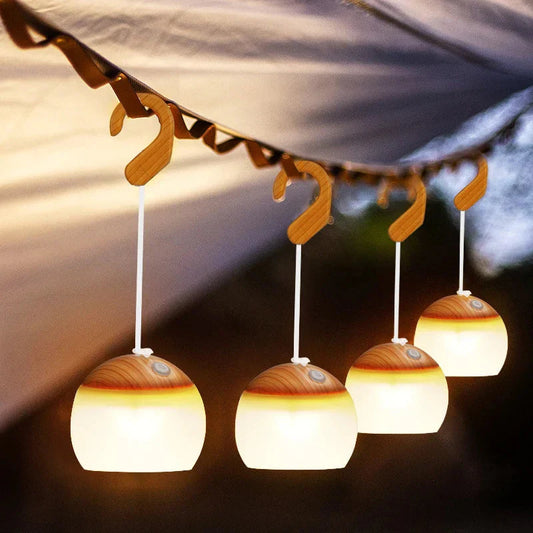 Vier hängende LED-Campinglampen, warmweiß, mit Holzaufhängung unter Zeltplane.