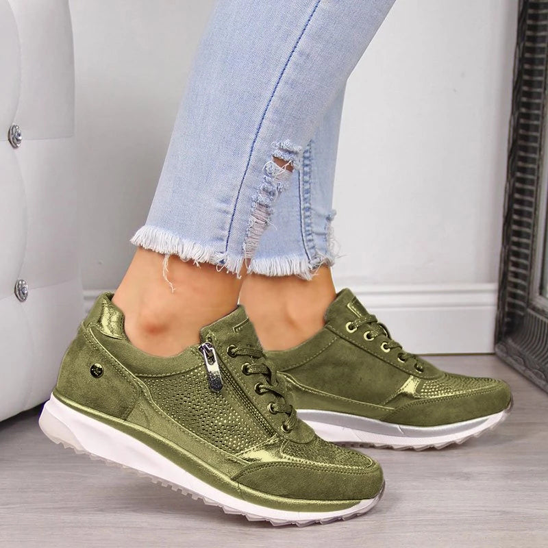 Getragener Sneaker in Olivgrün mit seitlichem Reißverschluss, Schnürung und glänzenden Akzenten, dazu helle Jeans mit ausgefransten Beinabschlüssen. 3