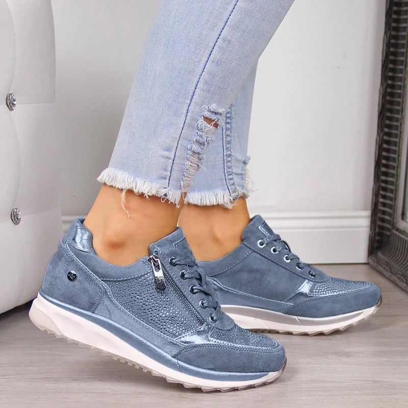 Blaue Sneaker mit Reißverschluss und Strasssteinen an den Füßen einer Frau in zerrissenen Jeans 3