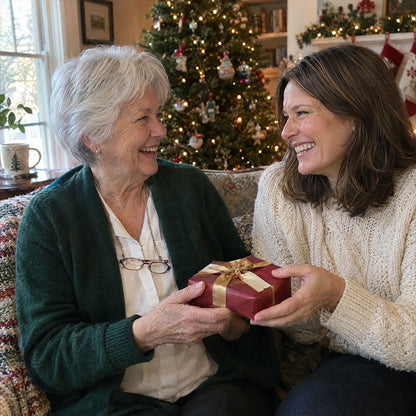 Zwei lächelnde Frauen auf dem Sofa vor dem Weihnachtsbaum überreichen sich ein rot verpacktes Geschenk mit Goldschleife 4
