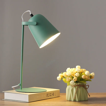 Grüne Tischlampe leuchtet auf einem Buch, daneben ein Väschen mit cremefarbenen Röschen vor grauer Wand. 9