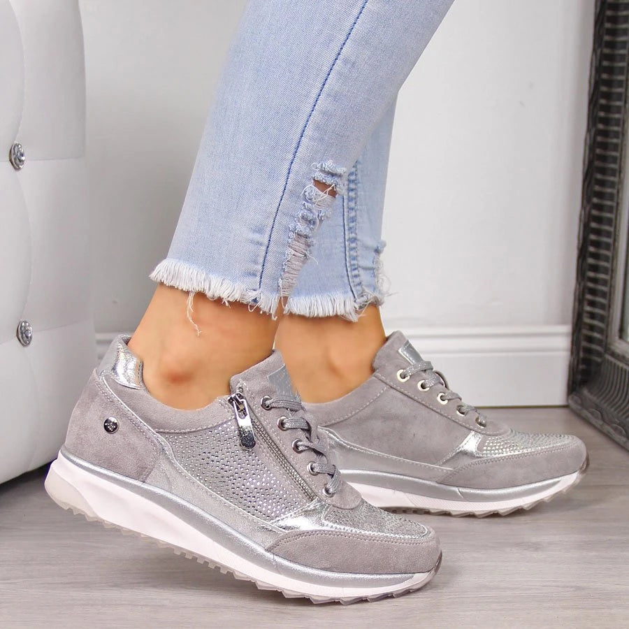 Getragener Sneaker in Grau mit silbernen Akzenten, Strassverzierung, Reißverschluss und weißer Sohle, dazu helle ausgefranste Jeans. 4