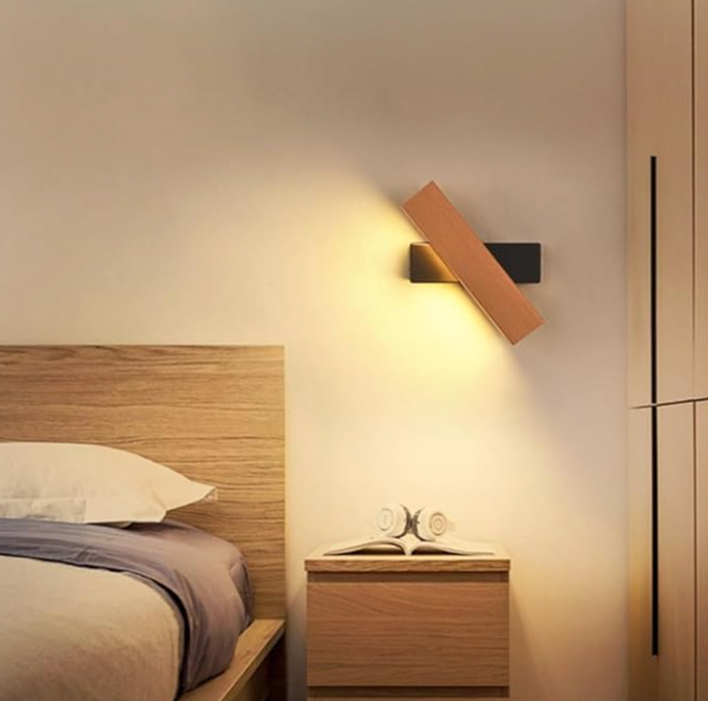 Wandleuchte mit Holzbalken und schwarzer Halterung neben dem Bett über einem Nachttisch.