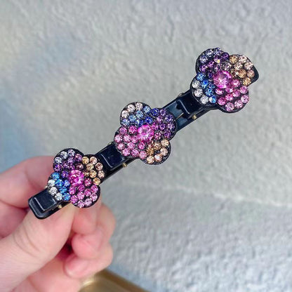 Detailansicht einer Haarspange mit drei bunten Strassblüten in Rosa, Blau, Lila und Gold, in der Hand gehalten. 5