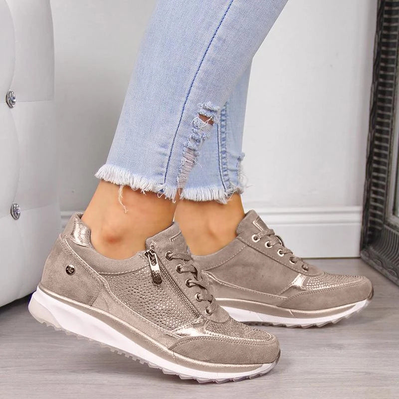 Getragener Sneaker in Taupe mit seitlichem Reißverschluss, Schnürung und perforiertem Glitzerdetail, kombiniert mit heller, ausgefranster Jeans. 1