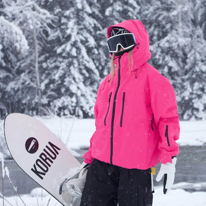 Neonpinke Skijacke mit Kapuze seitlich getragen, die Person hält ein Snowboard, Ärmeltasche und Brusttaschen mit Reißverschluss sichtbar. 5