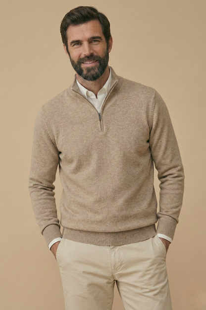 Lächelndes Model im beigen, melierten Strickpullover mit Stehkragen, beide Hände in den Taschen der hellen Hose 6