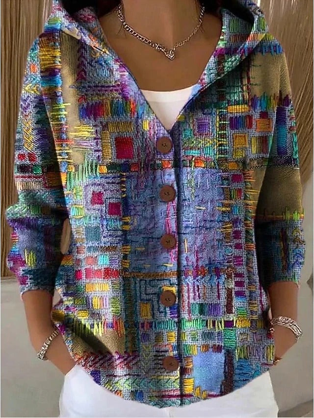 Frau trägt die Kapuzenjacke mit Knopfleiste in buntem Patchwork-Muster aus gestickt wirkenden Quadraten in Blau, Grün, Gelb und Rot. 1