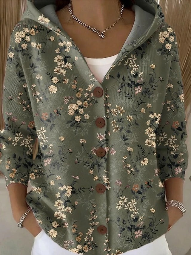 Graugrüne Kapuzenjacke mit Knöpfen, bedruckt mit feinen cremefarbenen und rosa Blüten an dunklen Zweigen, Frau mit Händen in den Taschen. 4