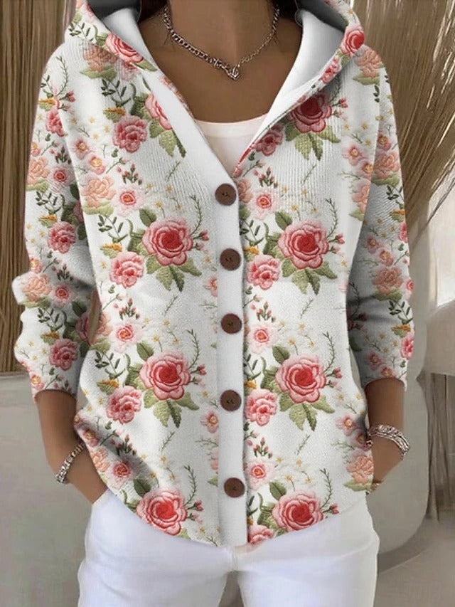 Weiße Kapuzenjacke mit großem Rosenmuster in Rot und Rosa mit grünen Blättern, kombiniert mit weißer Hose und braunen Knöpfen. 5