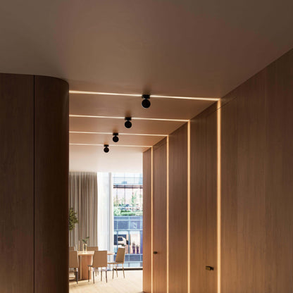 Schwarze Deckenleuchten in einer Reihe über einem Flur mit Holzwänden, mit schmalen Lichtlinien an Decke und Wänden. 15