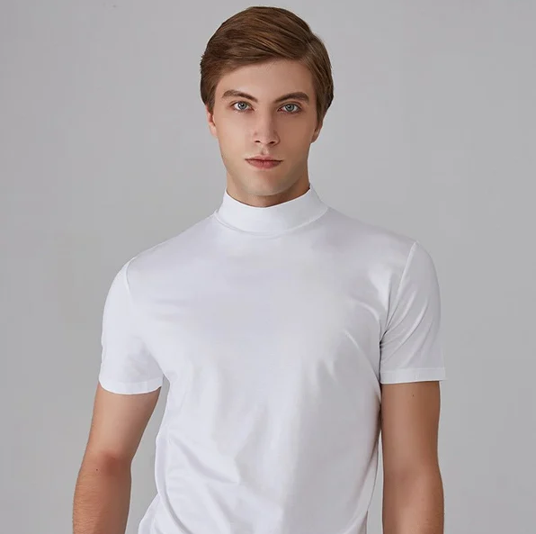 Model im weißen Kurzarmshirt mit Stehkragen blickt frontal in die Kamera, grauer Studiohintergrund, Oberkörper im Bild. 3
