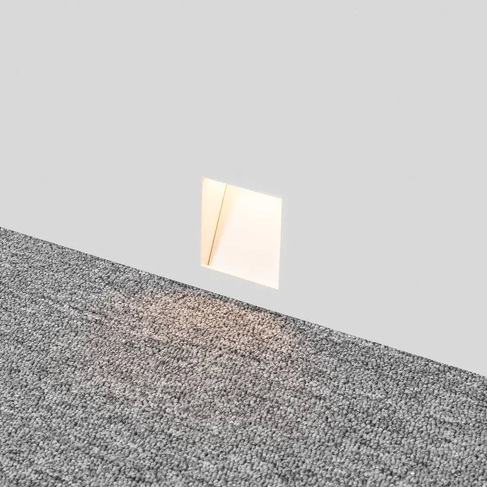 Eingebaute, leuchtende quadratische Wandleuchte knapp über dem Boden, Lichtschein auf grauem Teppich 3