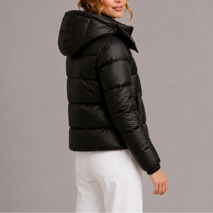 Rückansicht: Model in schwarzer Steppjacke mit Kapuze und elastischem Bündchen am Ärmel, dazu weiße Hose 4