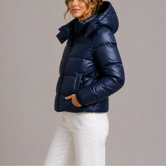 Seitenansicht: Model in marineblauer glänzender Steppjacke mit Stehkragen, Hand in der Tasche, dazu weiße Hose 1