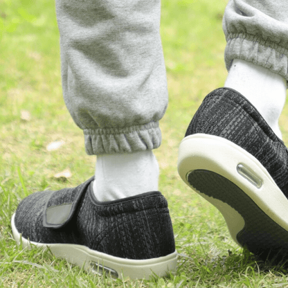 Schwarze orthopädische Schuhe mit Klettverschluss auf Gras, graue Jogginghose, weiße Socken.