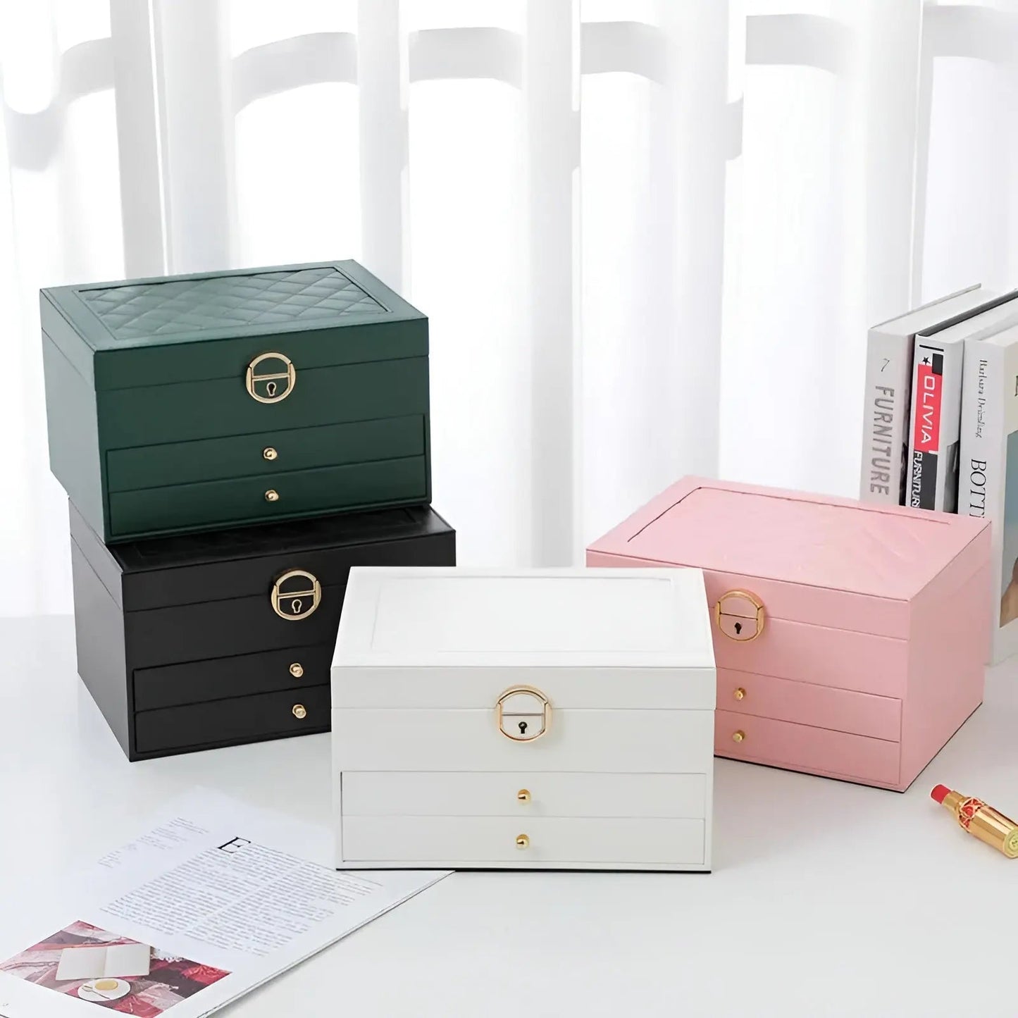 Vier Schmuckkästchen in Grün, Schwarz, Weiß und Rosa, mit Schubladen und goldenen Griffen.