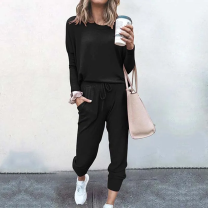 Frau in schwarzem Jogginganzug mit Kaffeebecher und rosa Tasche, lässige Mode.