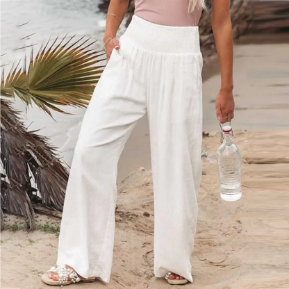 Frau in weißen Leinenhosen am Strand, hält Wasserflasche, Sommermode, lässiger Look.