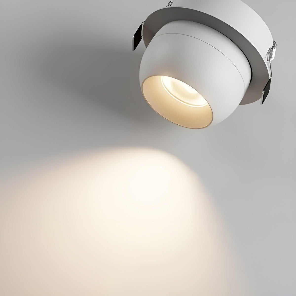 Nahaufnahme eines weißen Einbaustrahlers mit sichtbaren Federklammern und warmem Lichtkegel auf der Wand 4