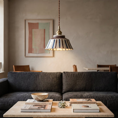 Keramik-Pendelleuchte mit gestreiftem Schirm über einem Couchtisch.