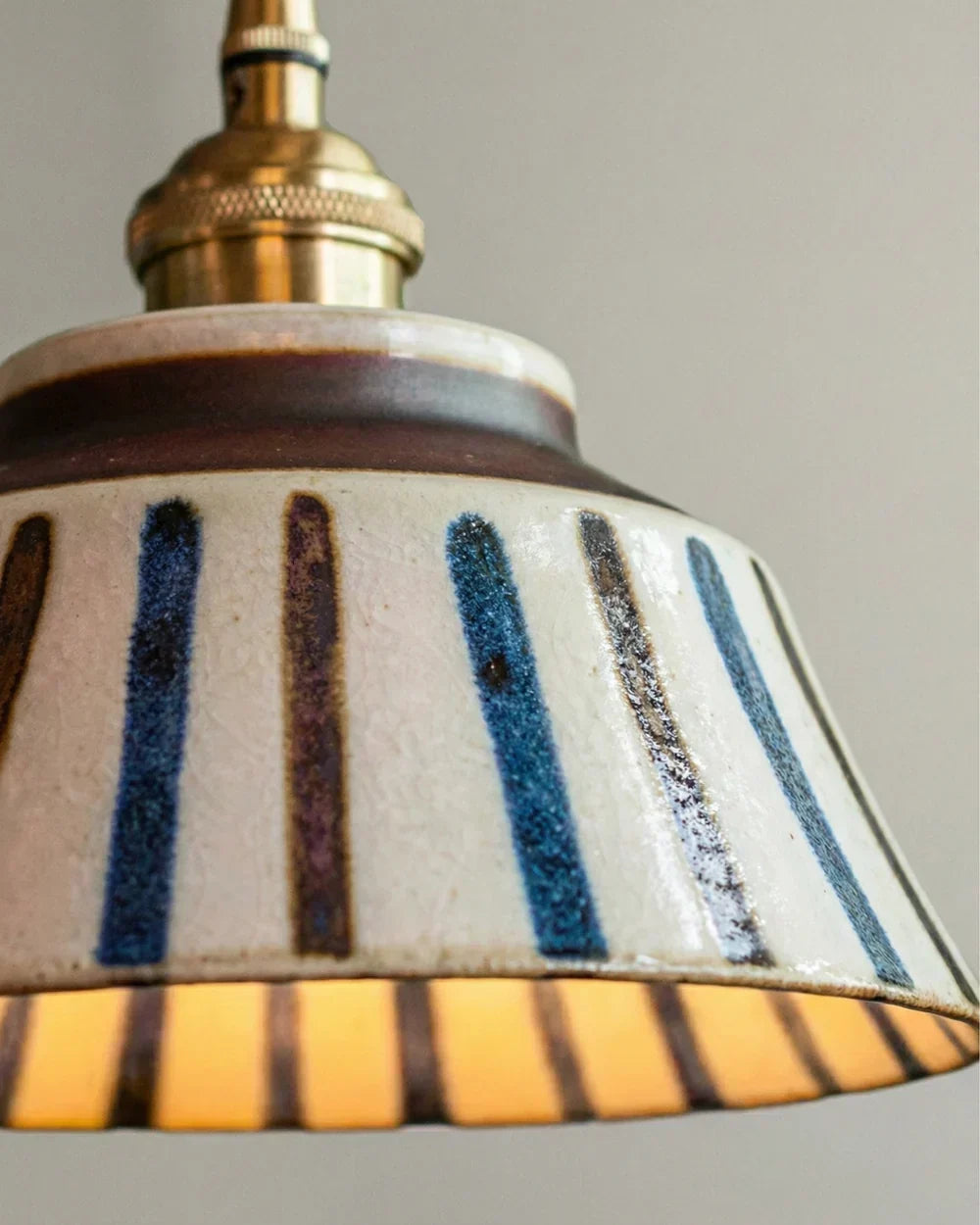 Detail der Keramik-Pendelleuchte mit gestreiftem Schirm und handgemalten blauen und braunen Strichen.