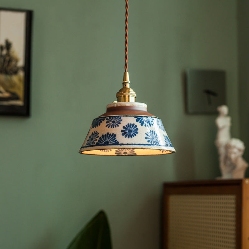 Keramik-Pendelleuchte mit blauem Blumenmuster und braunem Stoffkabel vor grüner Wand.