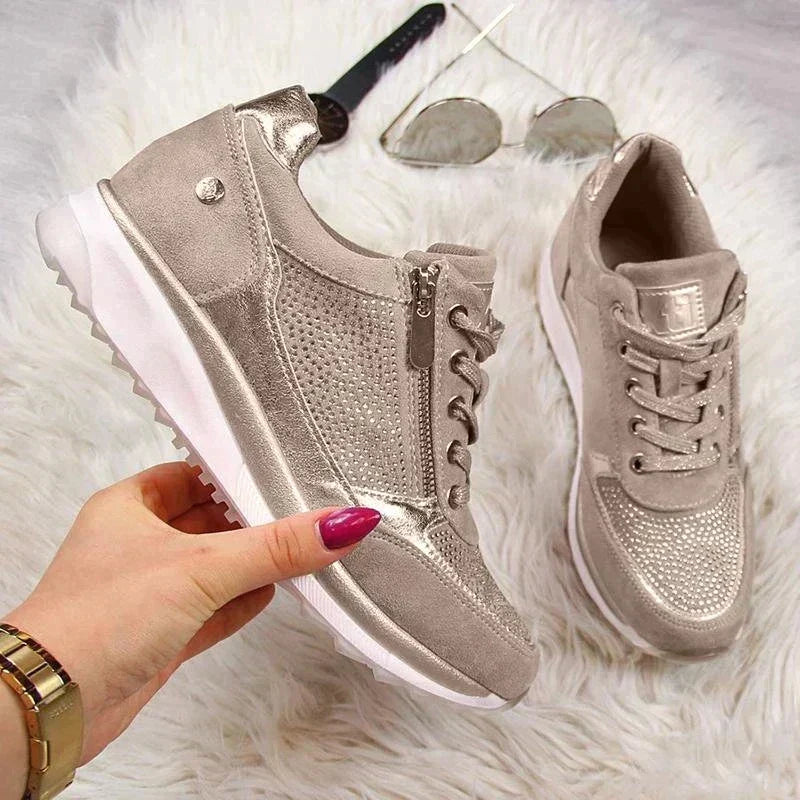 Beige Schuhe auf weichem Fell, ein Schuh von einer Hand gehalten, daneben Sonnenbrille und Armbanduhr.
