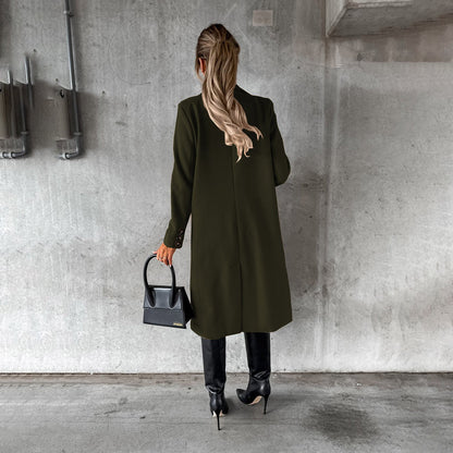 Frau in olivgrünem Wintermantel, schwarze Stiefel, schwarze Handtasche, Betonhintergrund.