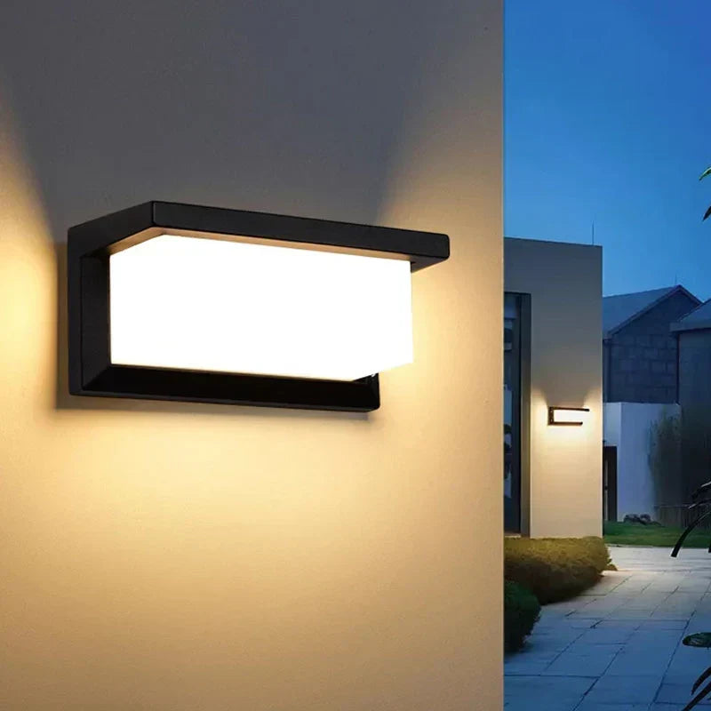 Wandleuchte in warmem Licht an einer Hauswand, im Hintergrund ein beleuchteter Gartenweg in der Dämmerung 3