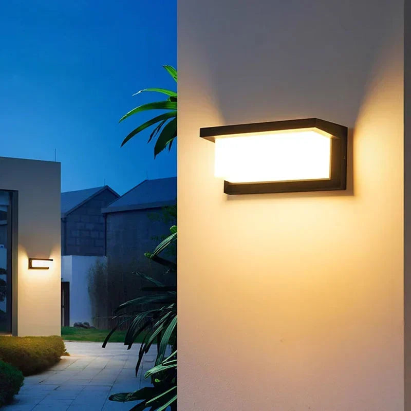 Eingeschaltete Wandleuchte an heller Hauswand, daneben Palmenblätter und ein weiteres Licht am Weg 4