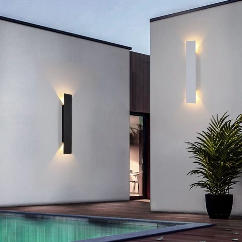 Eine schwarze und eine weiße zylindrische LED-Wandleuchte an hellen Außenwänden neben einem Pool.