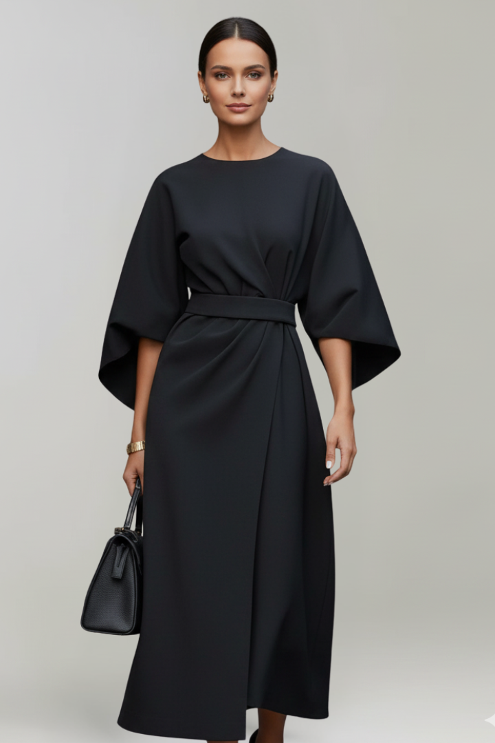 Model im schwarzen Kleid mit weiten Ärmeln und Taillengürtel, dazu eine schwarze Handtasche 7