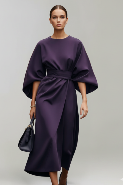 Model im dunkelvioletten Kleid mit weiten Ärmeln und Taillengürtel, dazu eine dunkle Handtasche 9