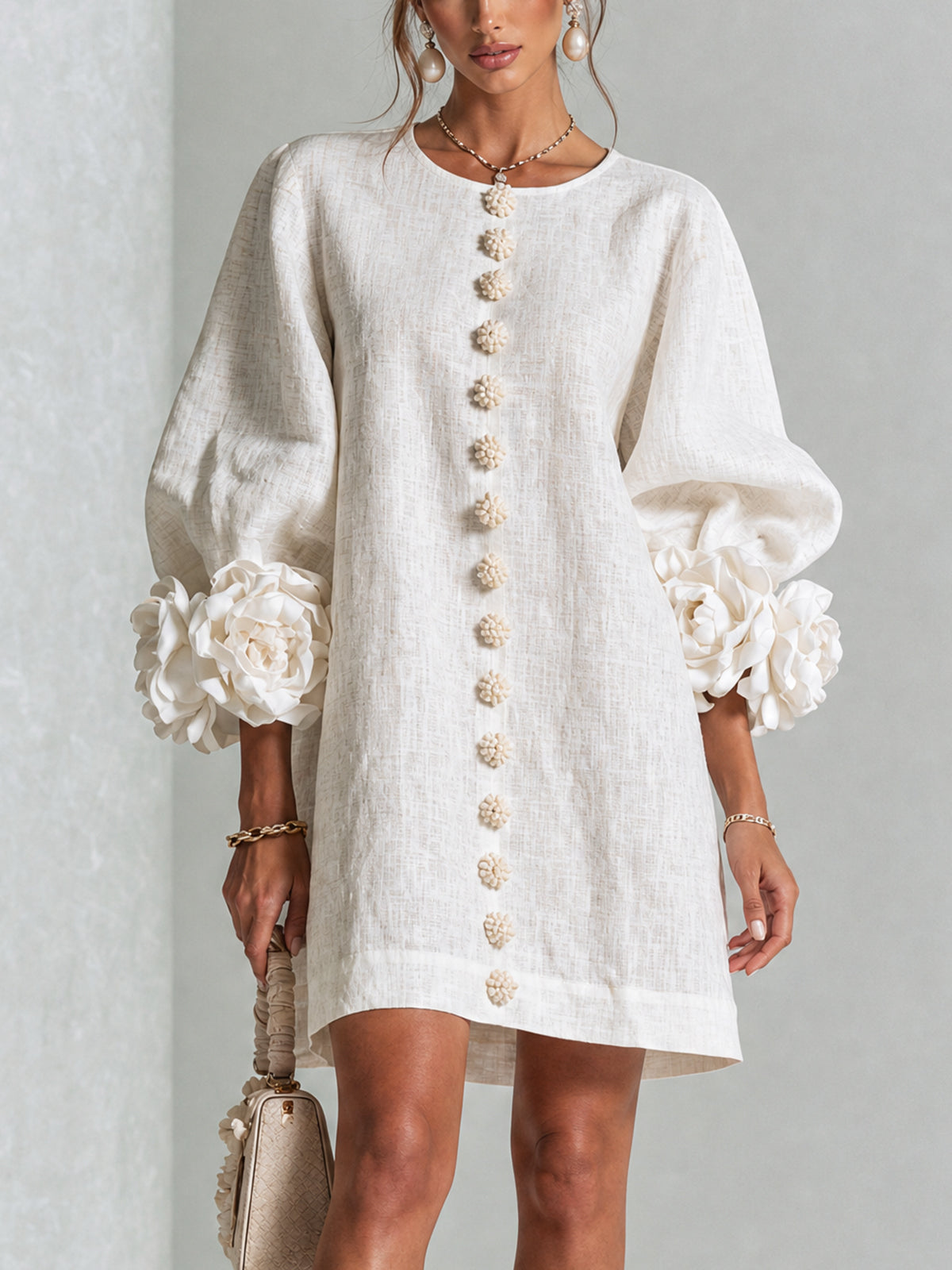 Model trägt das cremeweiße Kleid von vorn, mit Blütenknöpfen und großen Stoffblüten an den Ärmeln 1