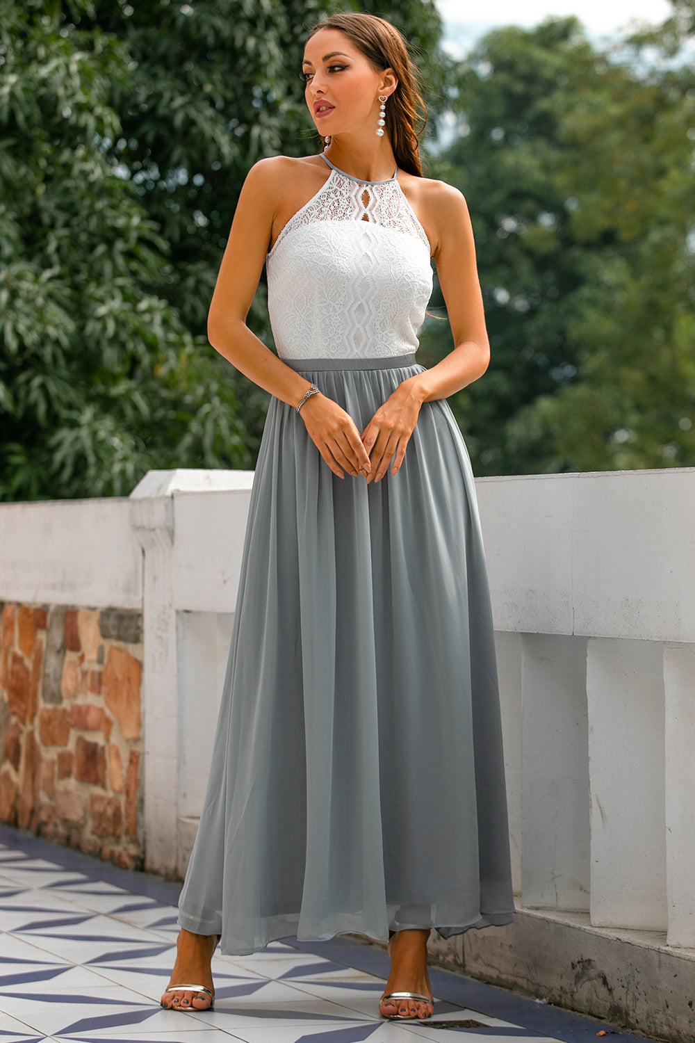 Frau im eleganten, ärmellosen Kleid mit weißem Spitzenoberteil und grauem Chiffonrock.