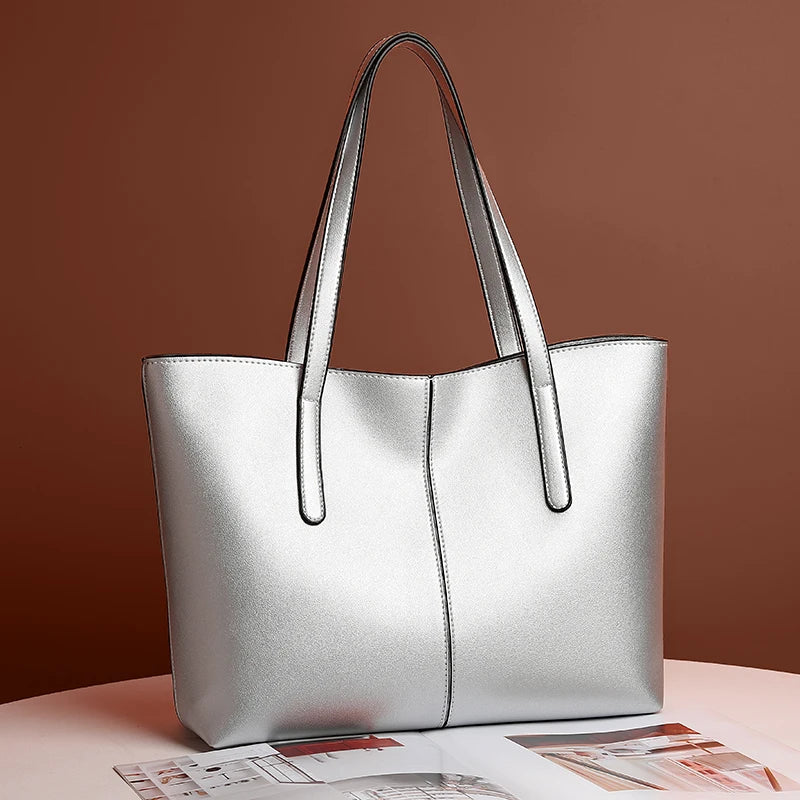 Silberfarbene Tote-Tasche schräg von vorn auf einem Tisch vor brauner Wand, daneben aufgeschlagene Zeitschrift 2