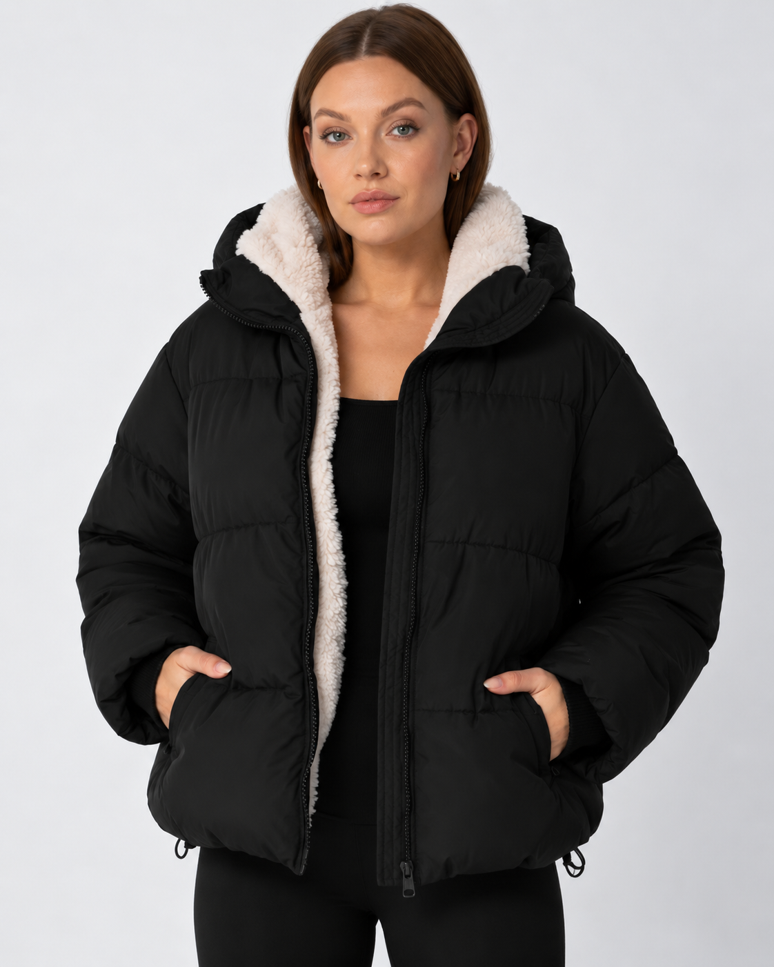 Model in schwarzer Steppjacke mit cremefarbenem Teddyfleece-Futter, Hände in den Taschen, Frontansicht 11