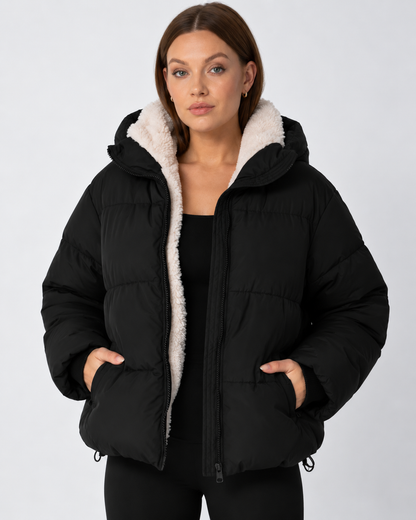 Model in schwarzer Steppjacke mit cremefarbenem Teddyfleece-Futter, Hände in den Taschen, Frontansicht 11