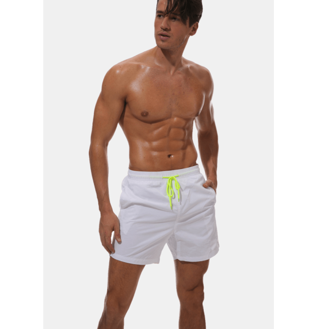 Weiße Herren-Badeshorts mit neongelber Kordel, getragen von einem Model mit nassem Oberkörper, eine Hand in der Tasche.