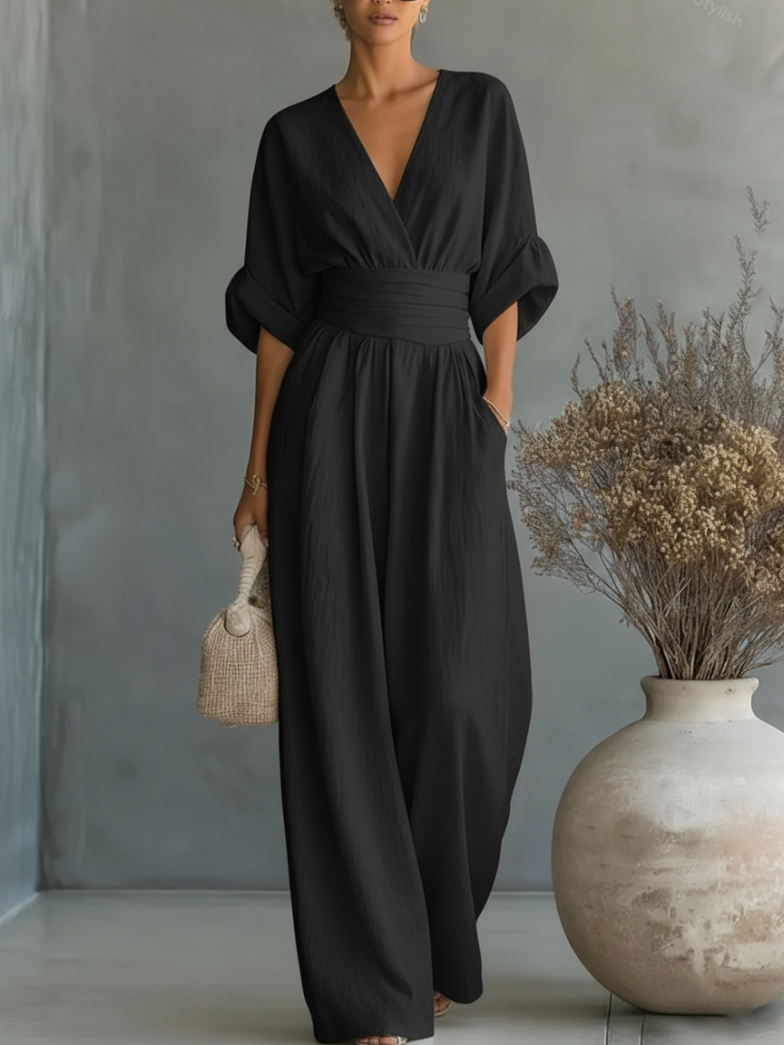Schwarzer Jumpsuit am Model, Ganzkörperansicht mit weiten, umgeschlagenen Ärmeln und Strohtasche 6