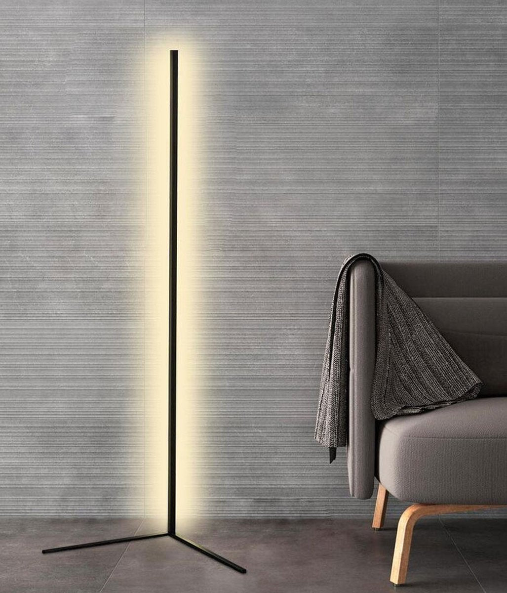 Schwarze LED-Stehlampe mit warmweißem Leuchtstreifen vor grauer Wandfläche neben einem Sofa mit Decke 8