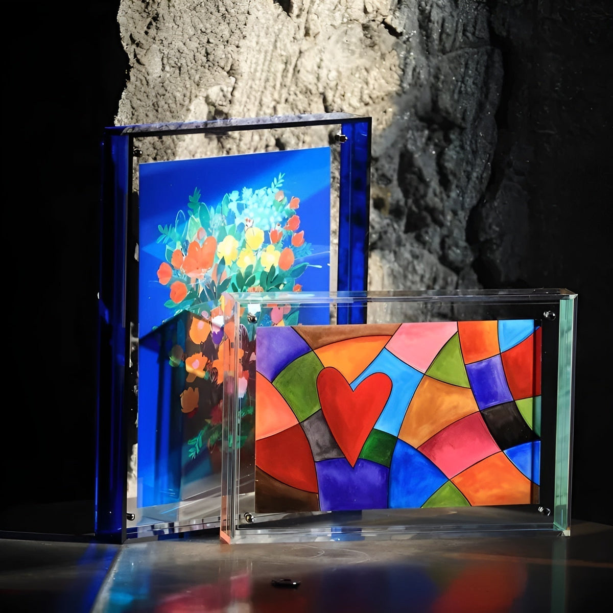 Blauer Acrylrahmen neben einem transparenten Querformat-Rahmen mit Herzmuster vor einer Steinwand