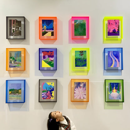 Neonfarbene Acrylrahmen an einer Wand mit bunten Bildern, darunter ein Kind