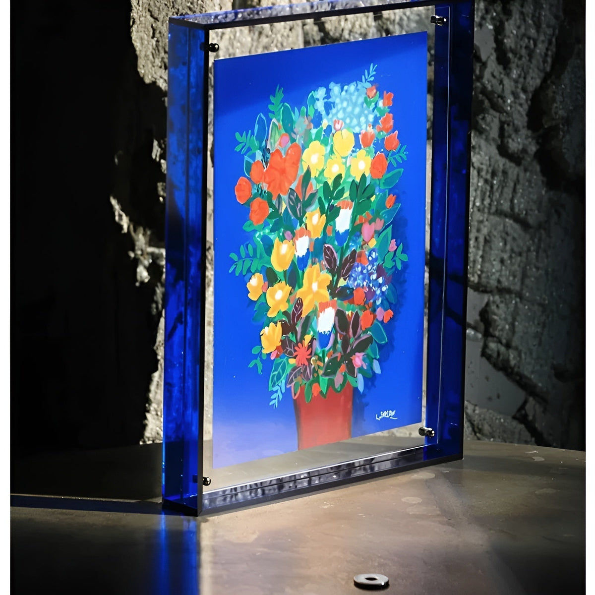 Tiefblauer Acrylrahmen mit Blumenstrauß-Druck vor einer Steinwand