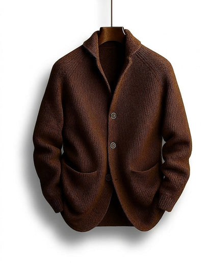 Braune Strickjacke mit Schalkragen, drei Knöpfen und aufgesetzten Taschen, frontal auf einem Holzbügel hängend. 1